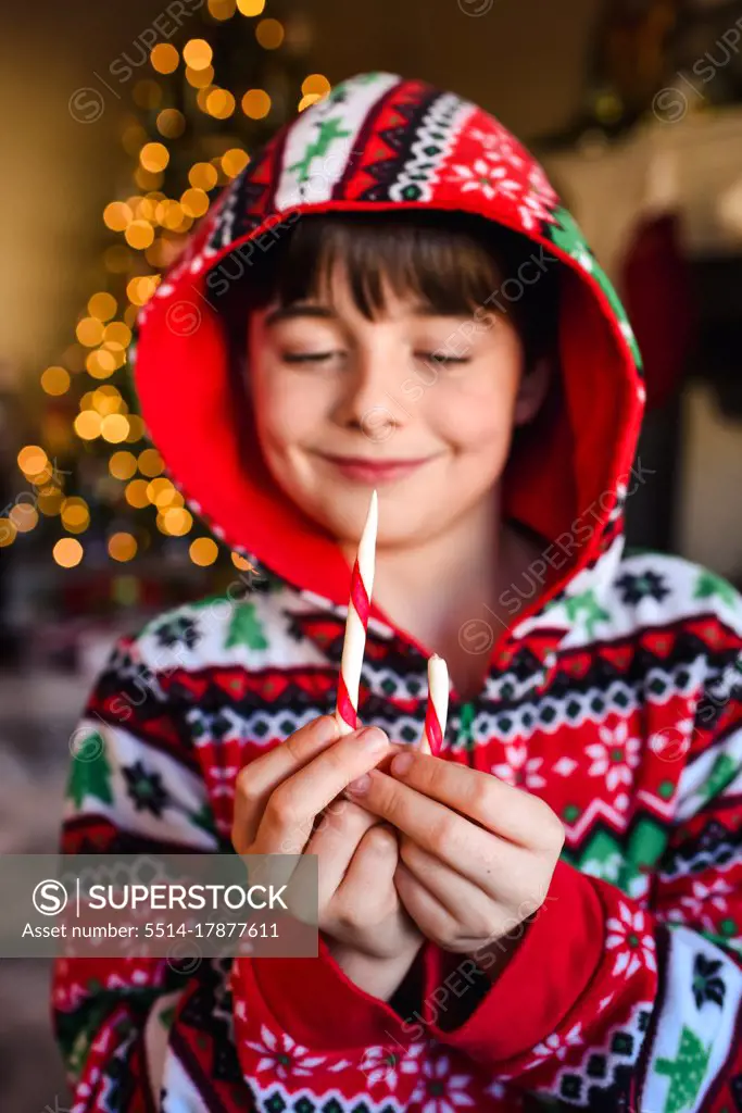 Cute boy in festive pajamas eating a candy cane at Christmas time.