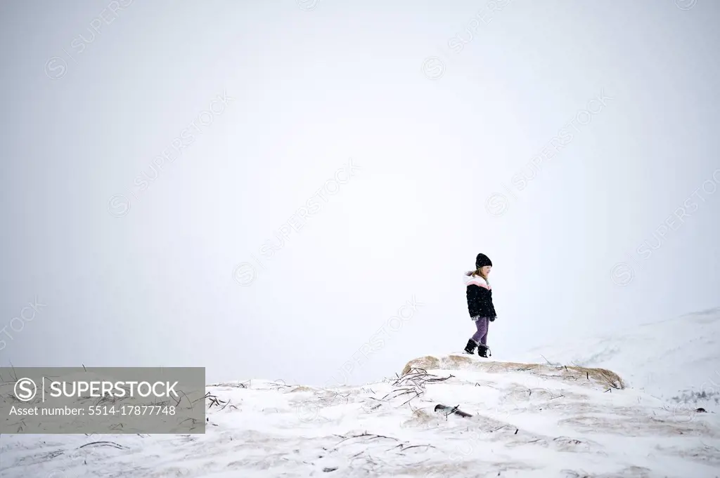 Unrecognizable kid in warm clothes walking on snowy mountain slope