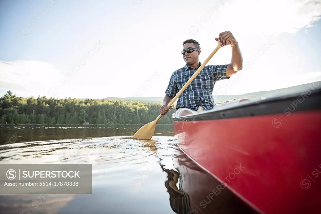 Black man paddles red canoe on calm serene Bald Mountain Pond Maine