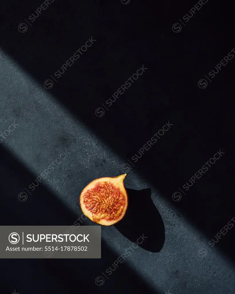 Minimal photo of a fig half on dark background in a ray of light