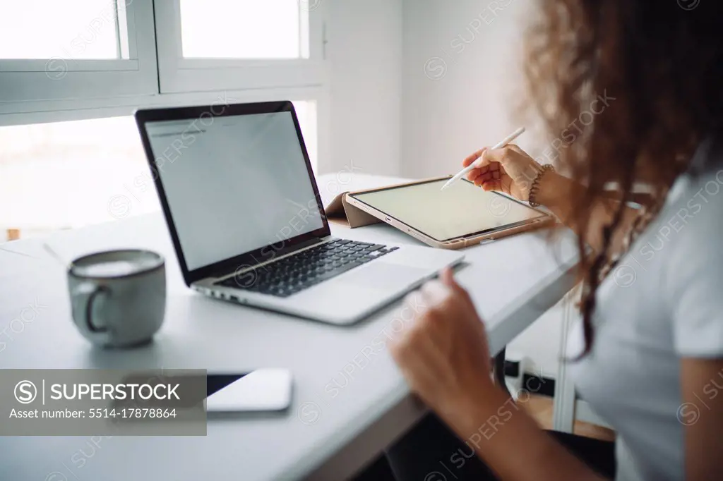 Young woman working from home using a laptop, a smarphone and a tablet while having a coffee