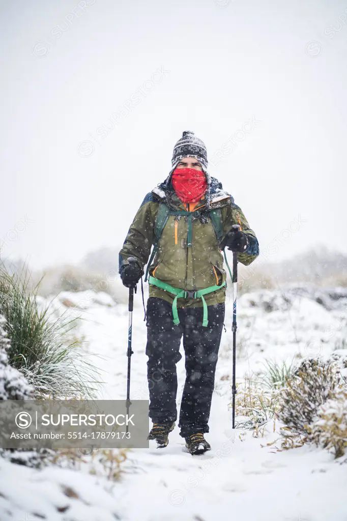 A man with face covered treks under heavy snow