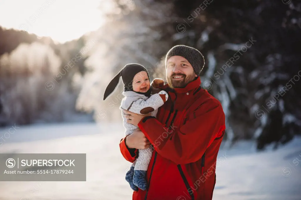 Father and baby smiling in winter wonderland full of snow in the woods