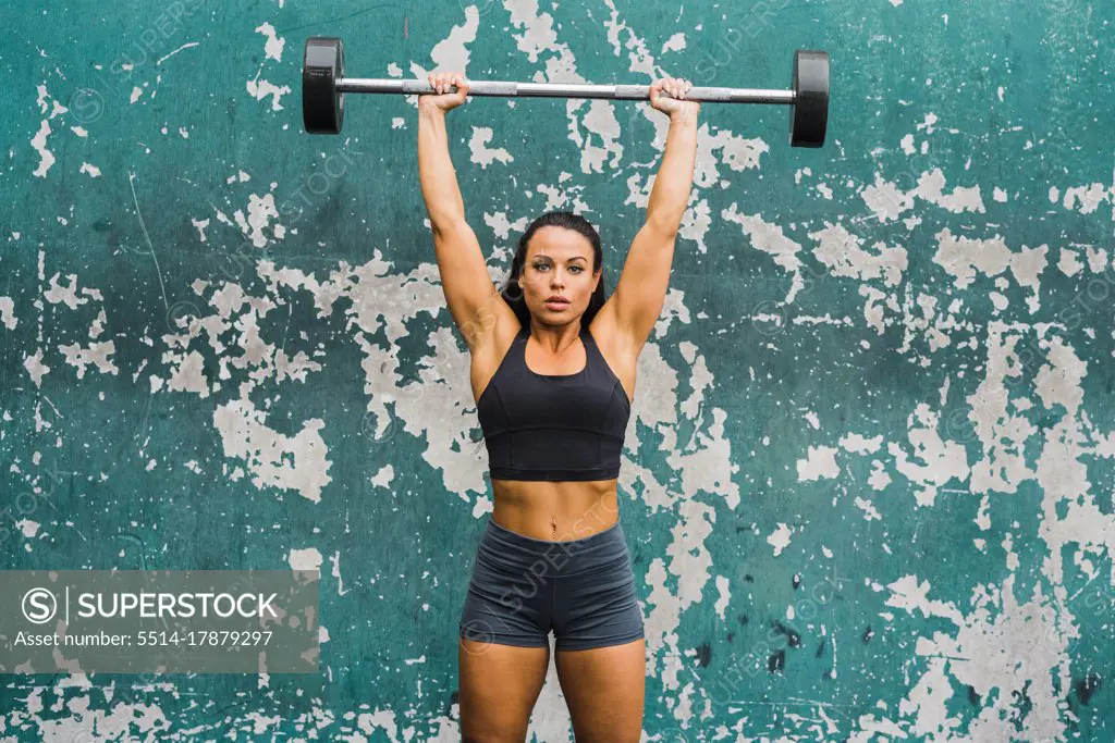 female athlete performing shoulder press at wall of outdoor gym