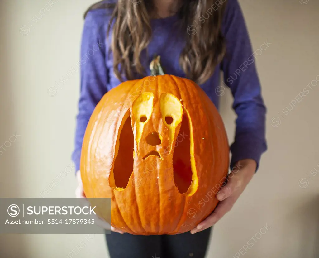 Close up of tween girl holding up carved pumpkin of dog against wall