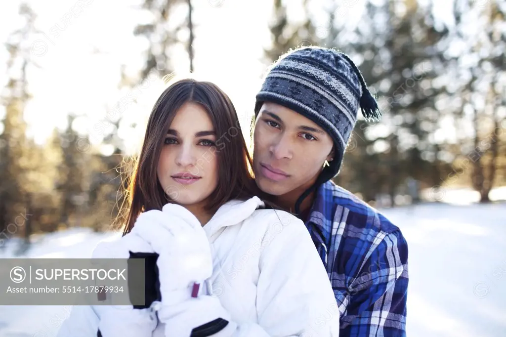 Couple embracing while looking at camera in snowy forest