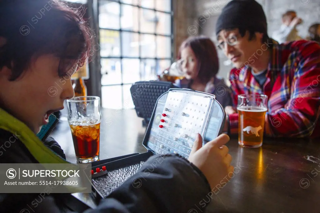 A little boy sits in a restaurant with sister and dad playing game