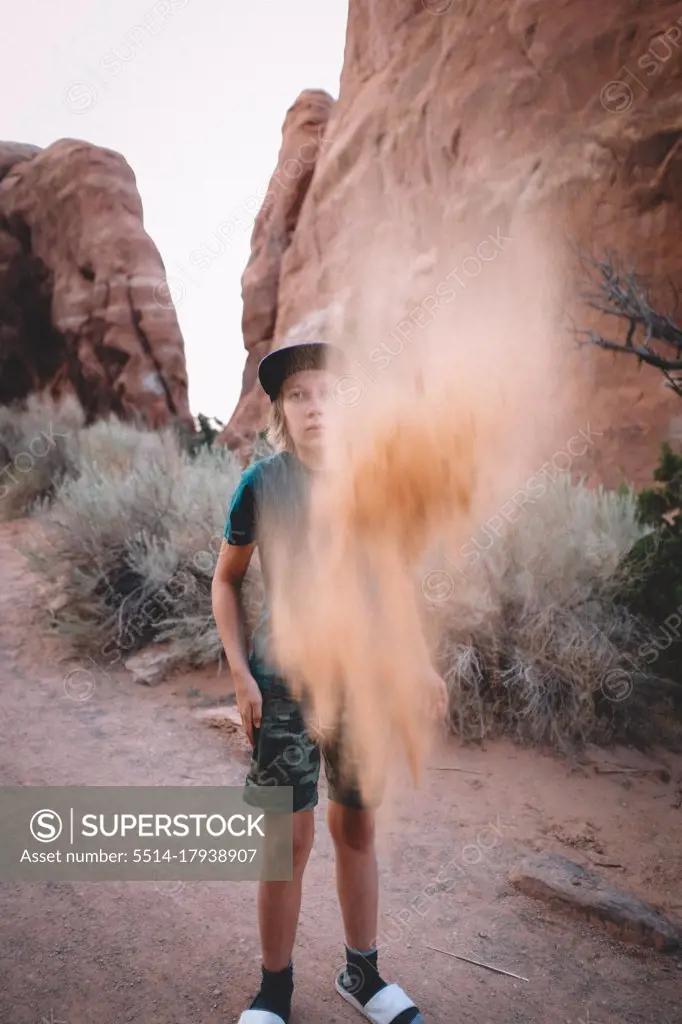 Boy Tosses Sand into the Air Surrounded by Sandstone and Desert