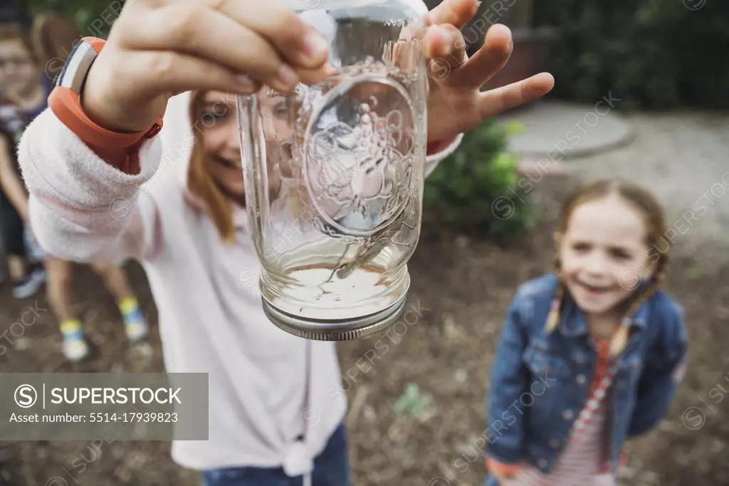 Excited kids holding up a jar with a cricket inside