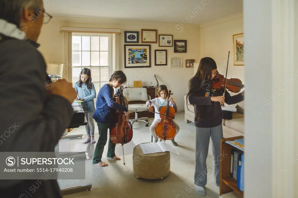 A group of children with stringed instruments play as father watches