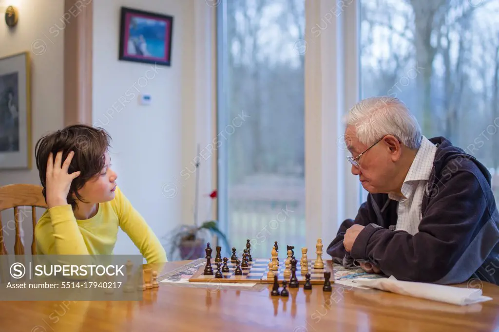 A grandfather carefully studies a chessboard while grandson looks on