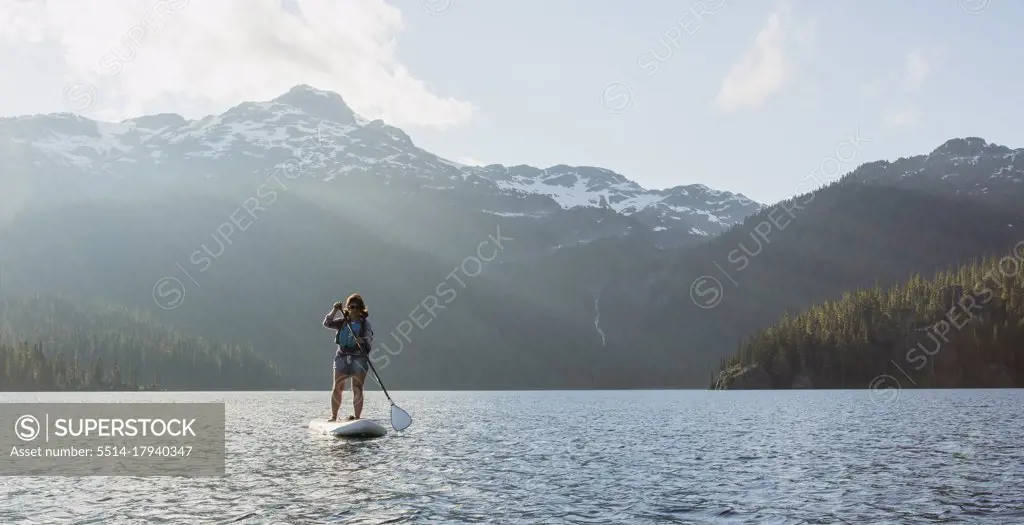 Female adventurer paddle boarding on lake against snowy mountain ridge