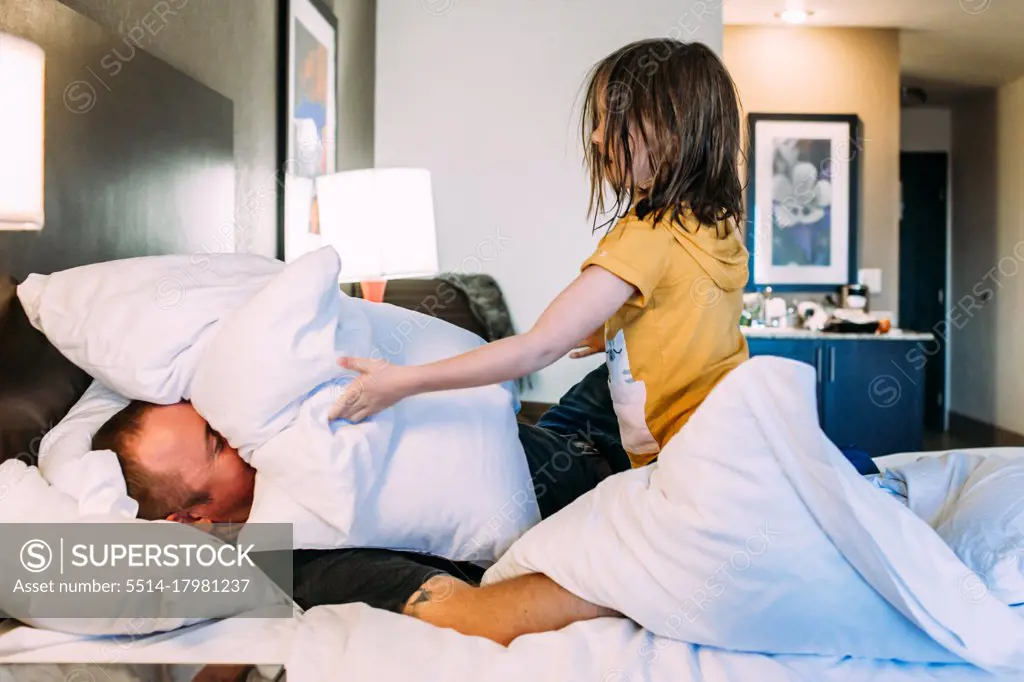 Happy young child playing with father on a bed in a hotel room