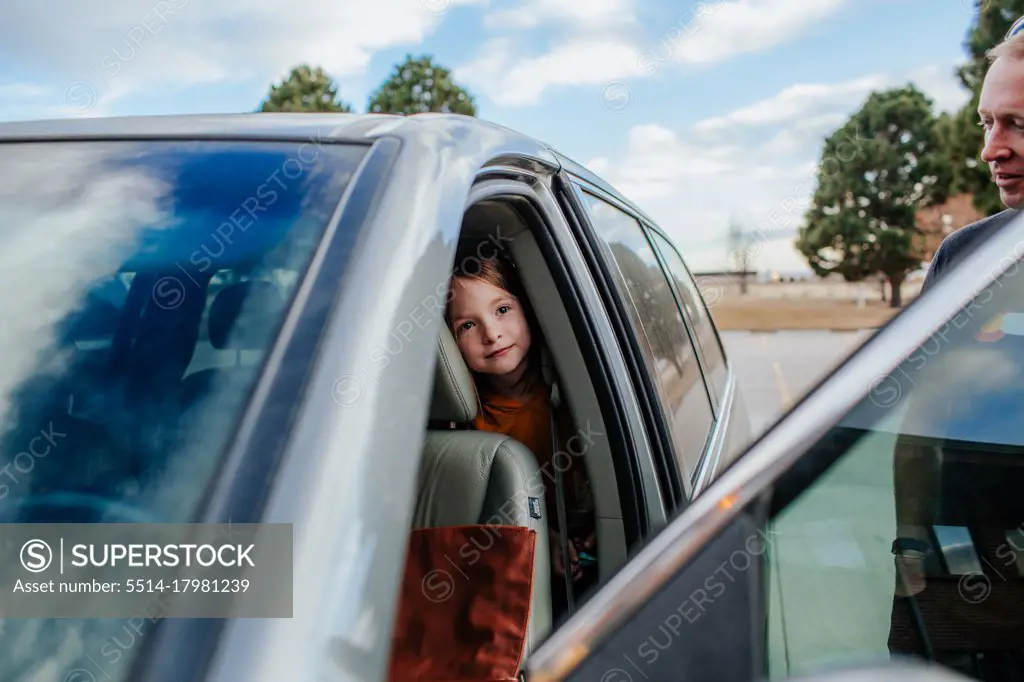 Young girl peeking out from back seat of a car before a trip