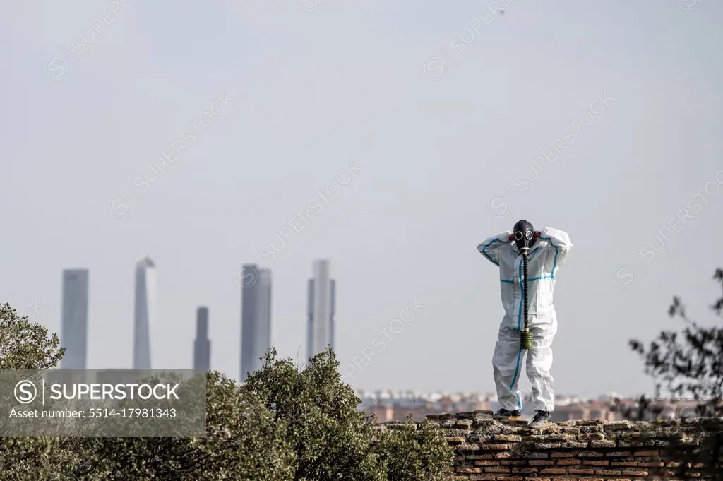 A man in a EPI virus suit and a gas mask on his face with the city in the background