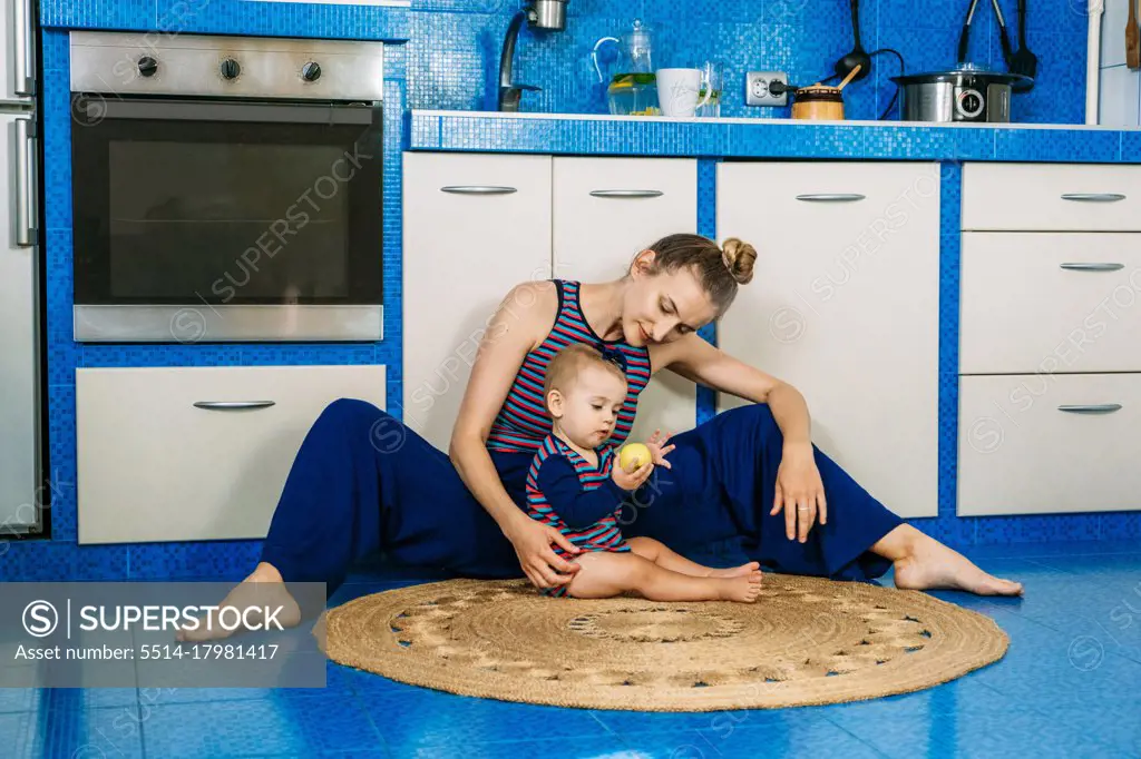 Young mom and her baby girl playing with apple in the kitchen