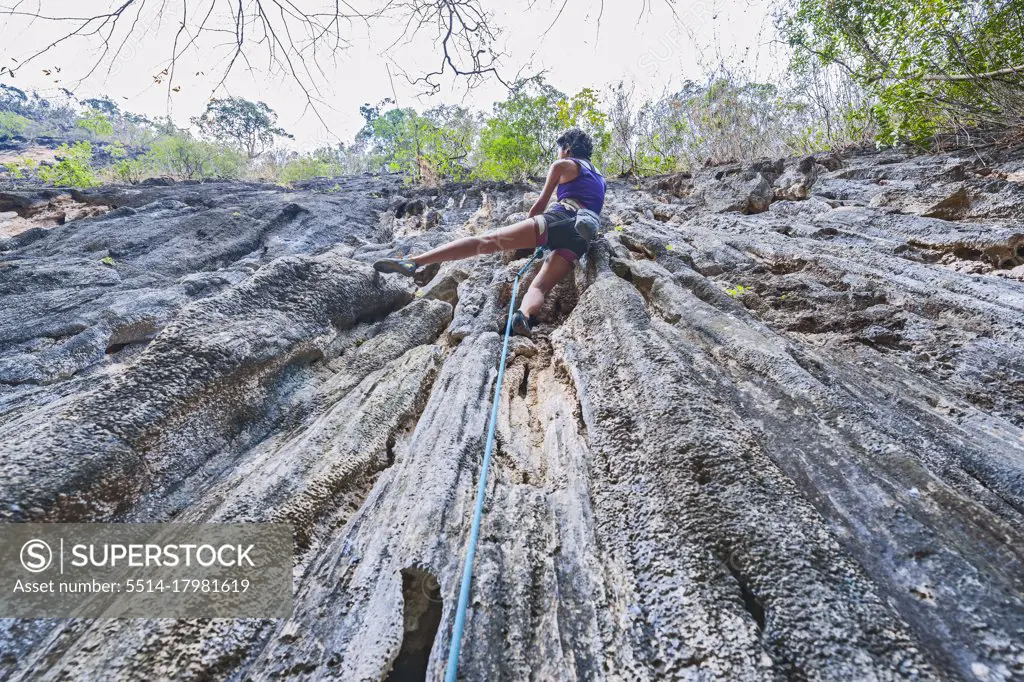 woman climbing steep limestone cliff in Laos