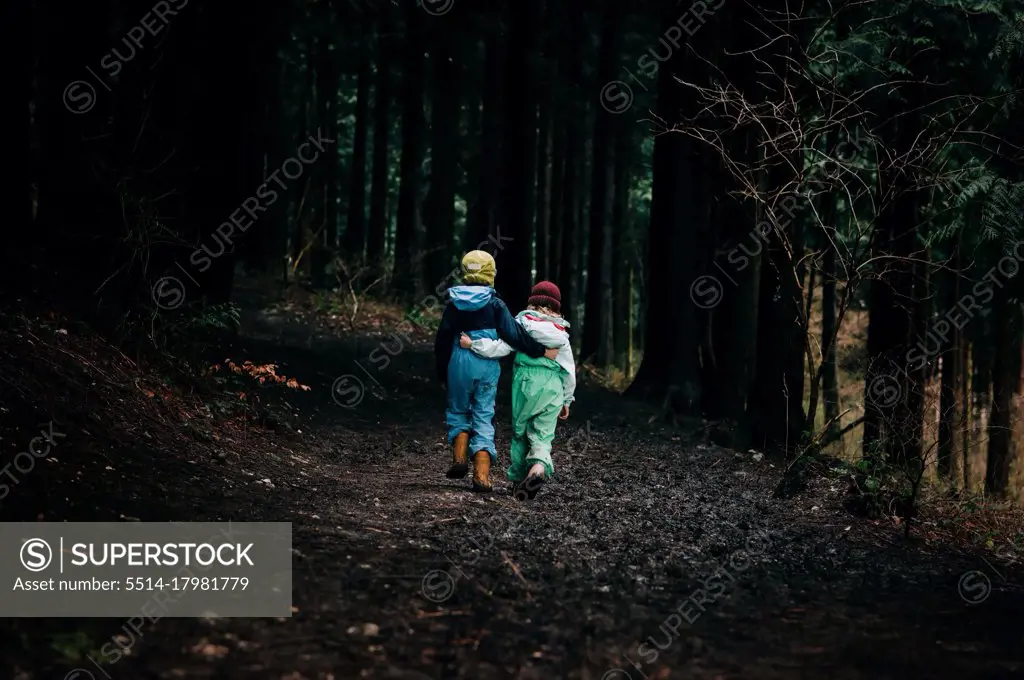 kids walking with their arms around each other into the dark forest