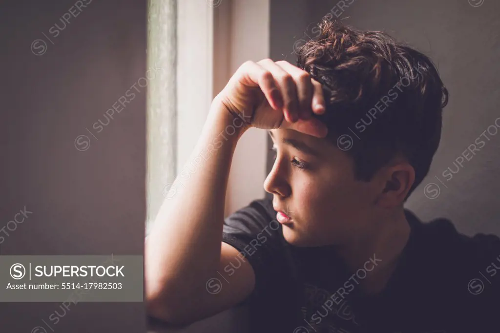 Boy leaning against the wall looking outside a window.