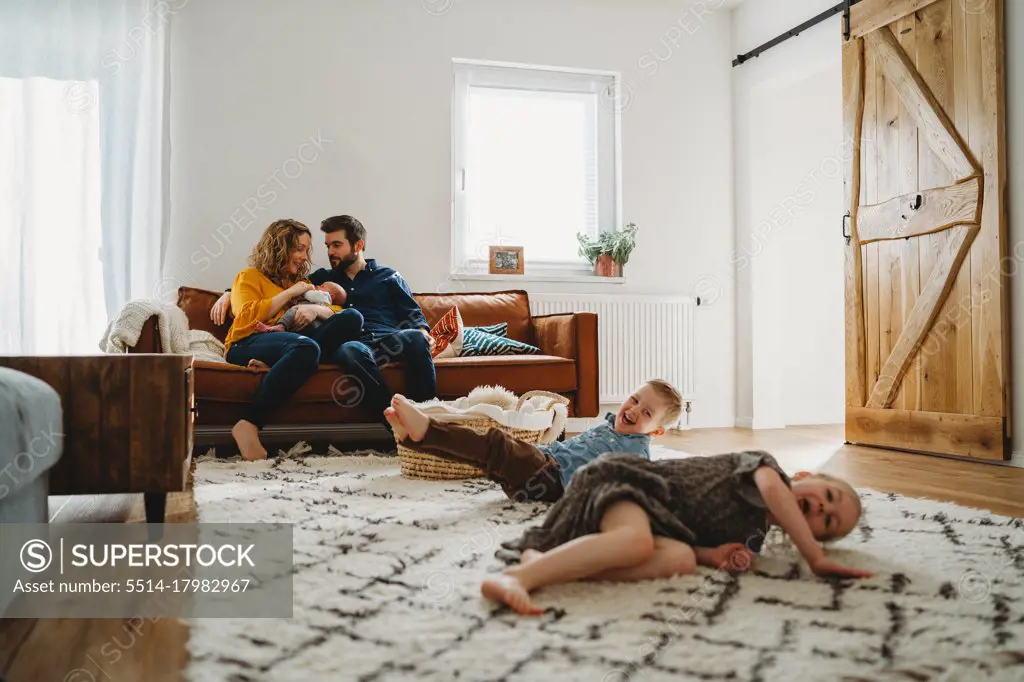 Siblings having fun in living room parents sit on sofa with baby