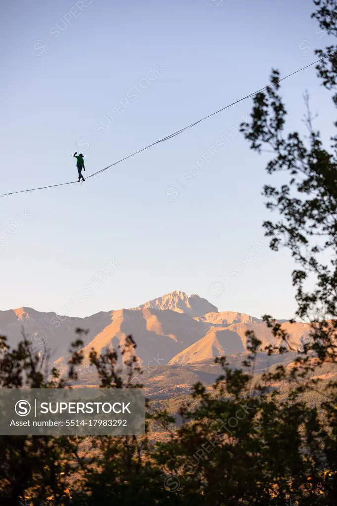 Slackliner walking over Gran Sasso with trees in the foreground