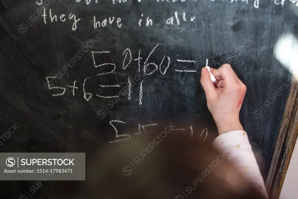 close-up of a small child writing mathematical equations on chalkboard