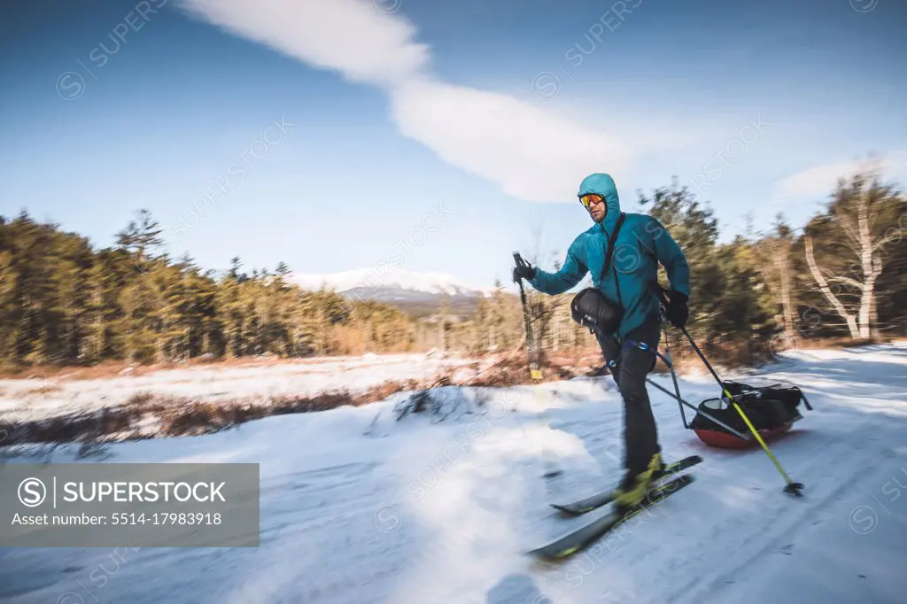 Man skis on snow covered trail towing sled, Katahdin, Maine