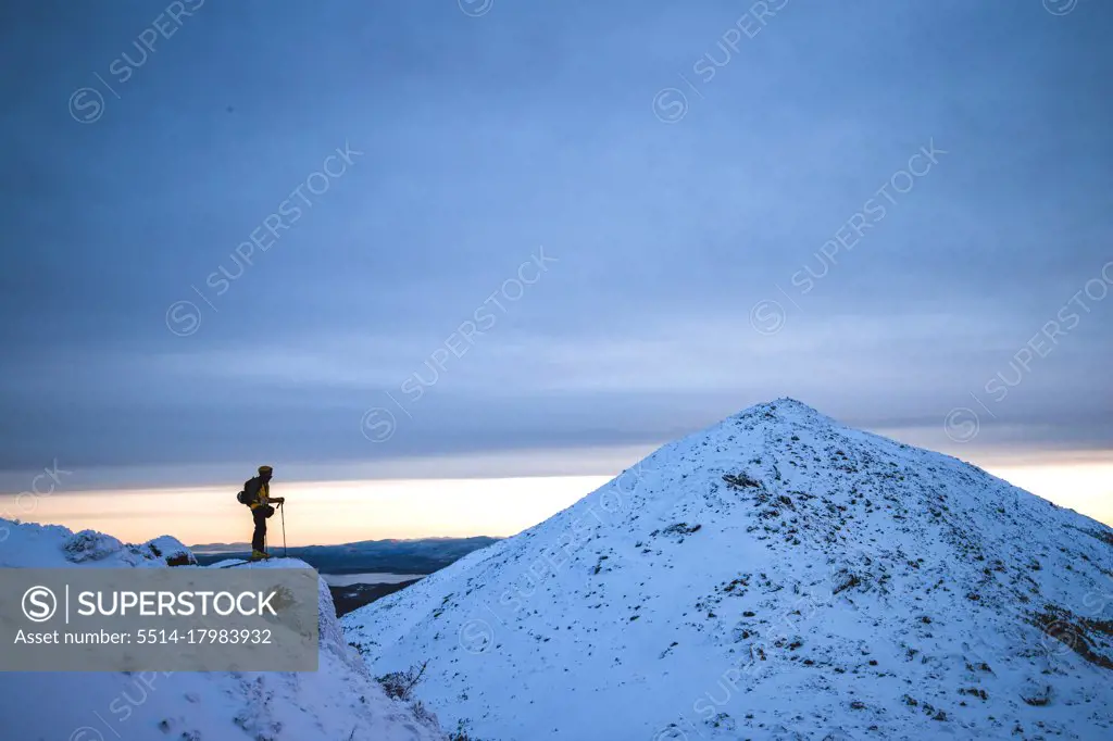 Man stands on cliff in snow in winter looking at distant mountain