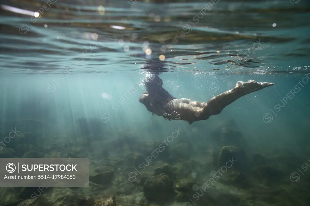 female swimming away from camera and up to surface of shallow ocean