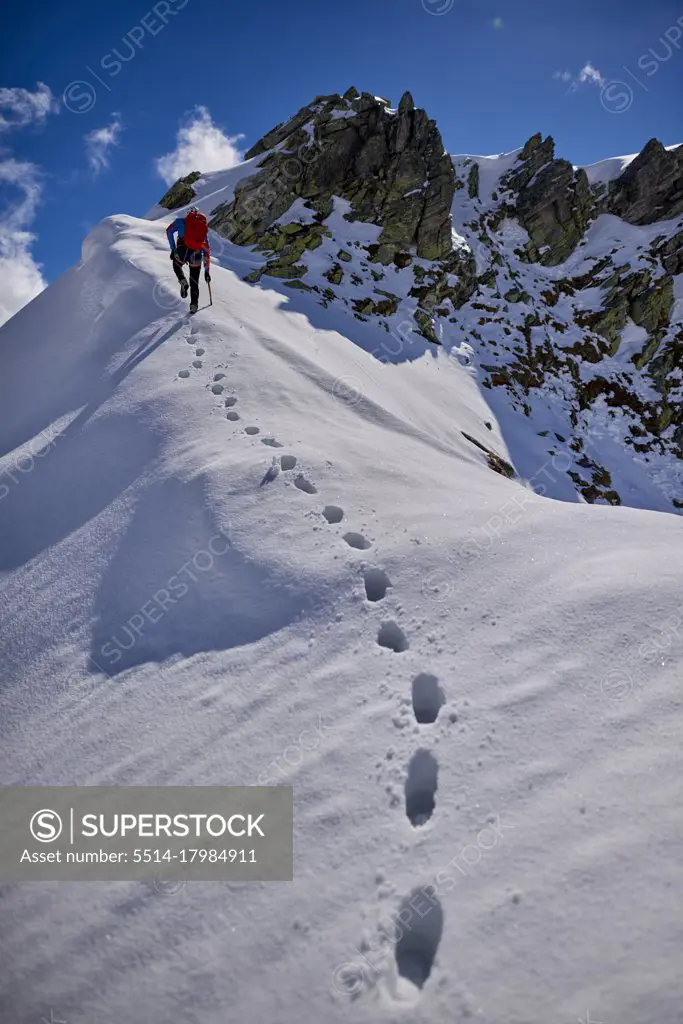 Man climbing a snowy mountain on a sunny day in Devero, Italy.