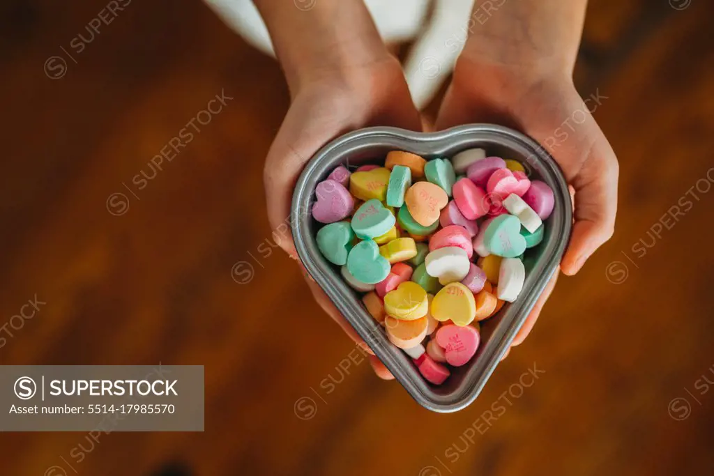 overhead of child's hands holding candy hearts in heart dish