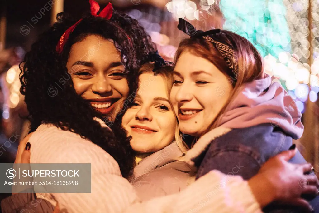 Close up portrait of happy female friends embracing in city at night