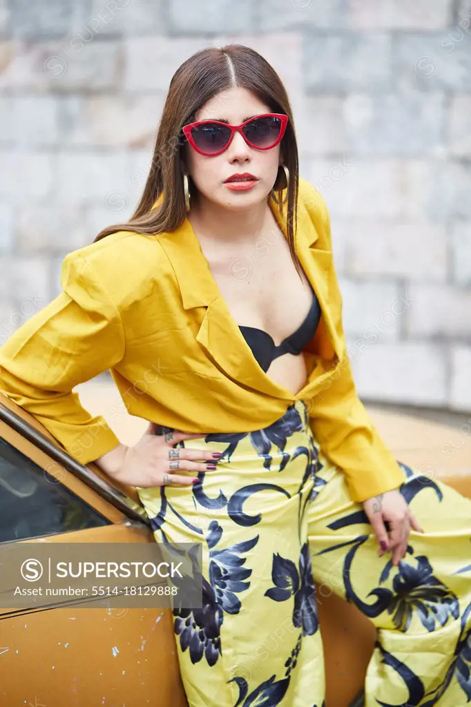 portrait of a young woman in a yellow dress leaning against a car