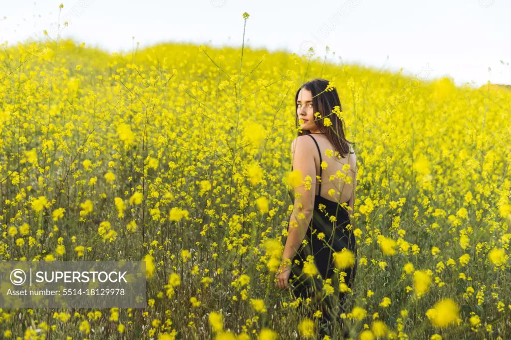 Young female adult looking back at camera in yellow wildflower field