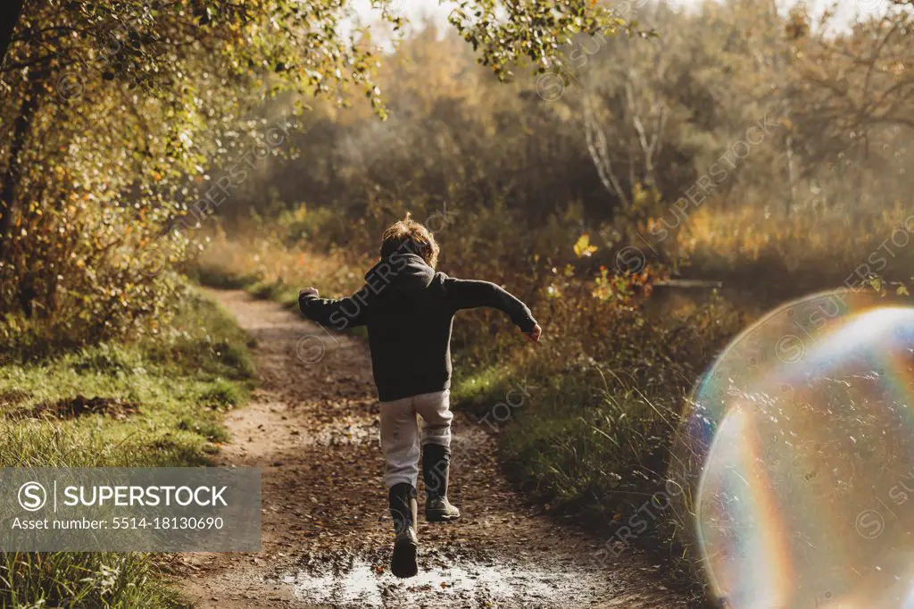 Rear view of boy jumping over muddy puddle on canal side path