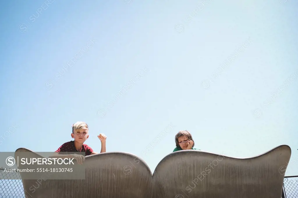 Boys Peek Over a Cement Whale Tale Bench on a Summer Day