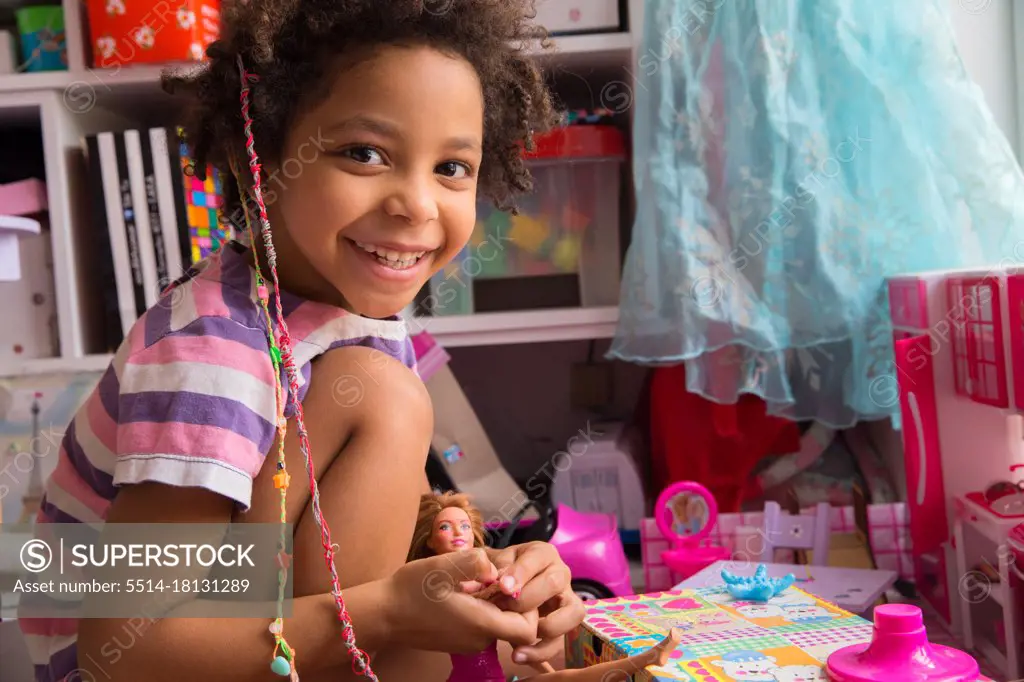 Mixed race little girl playing with doll smiling in a playroom