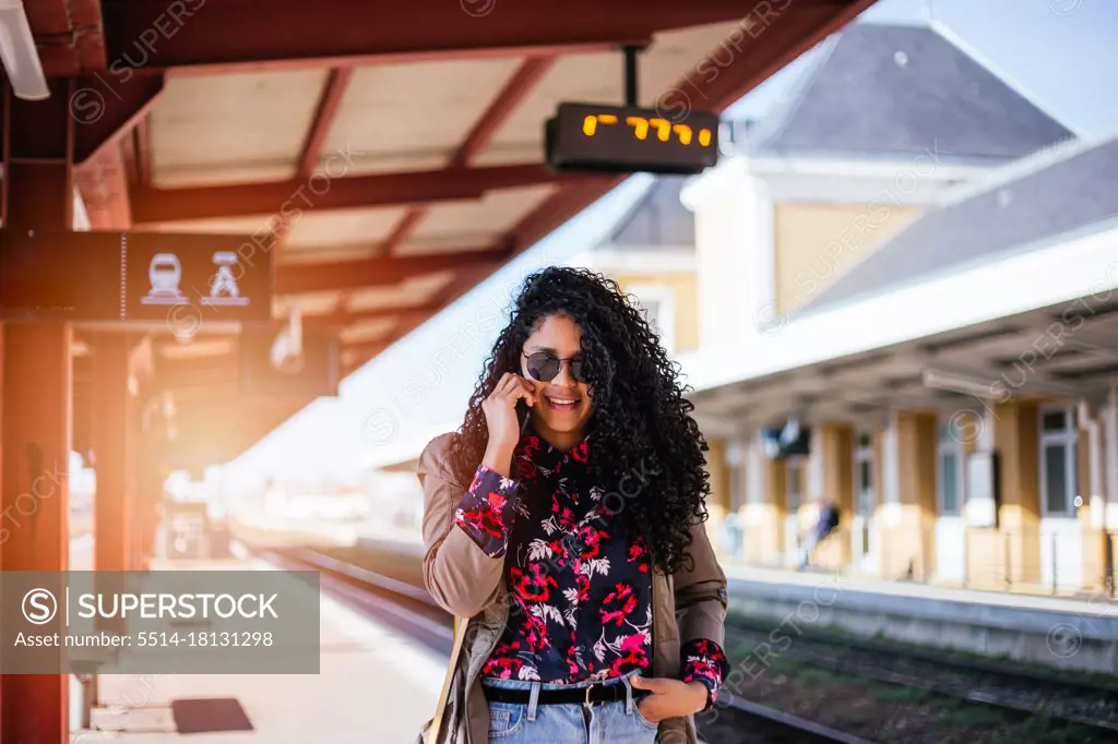 Happy young African girl talking on cell phone at train station in Europe