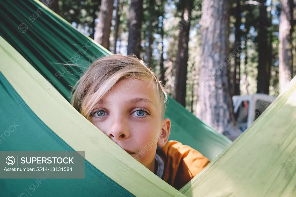 Blonde Tween with Big Blue Eyes Peeks from behind a Green Hammock