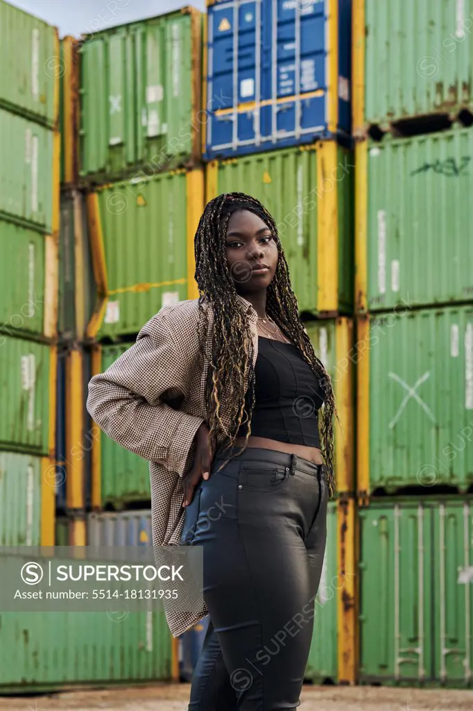 Black woman in urban clothing poses surrounded by shipping containers