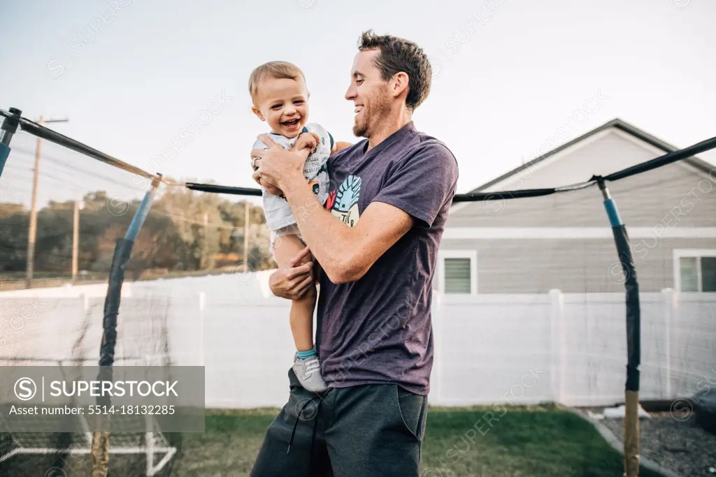 Dad laughing on trampoline with toddler son