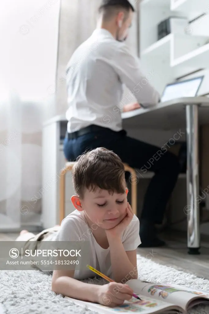 boy does homework near father working