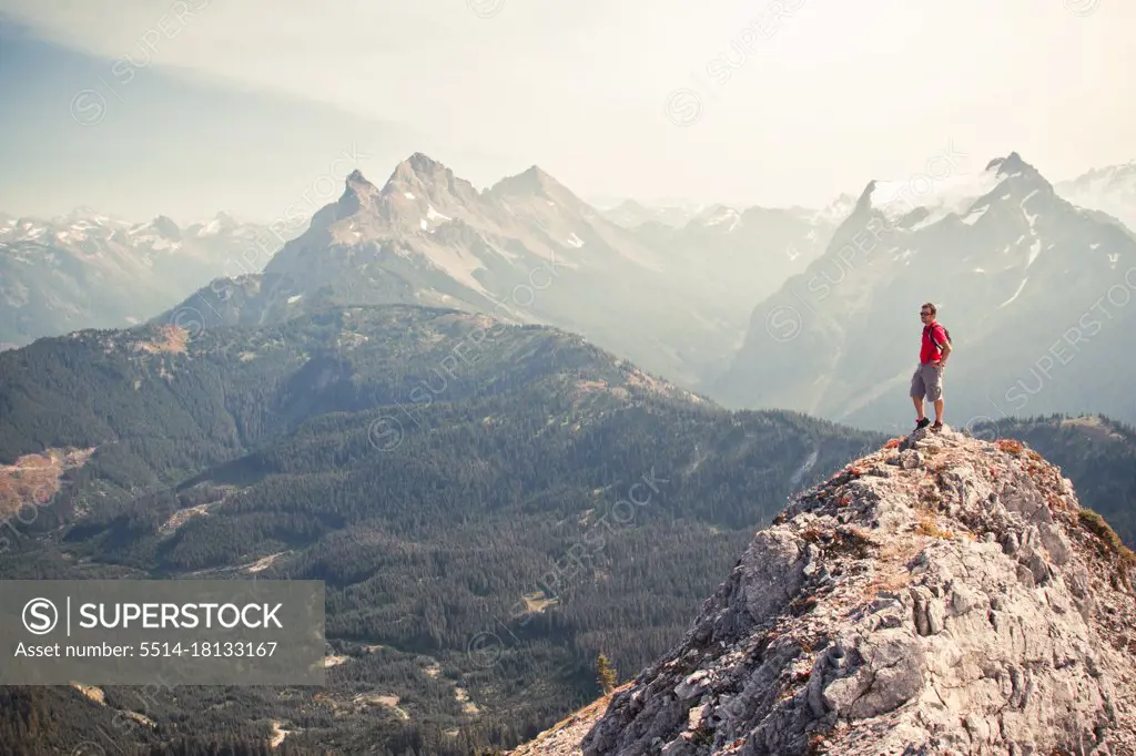 Man in red standing on summit looking out at the view.