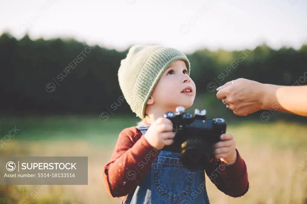 Little boy  holding film camera  in a large field in the country