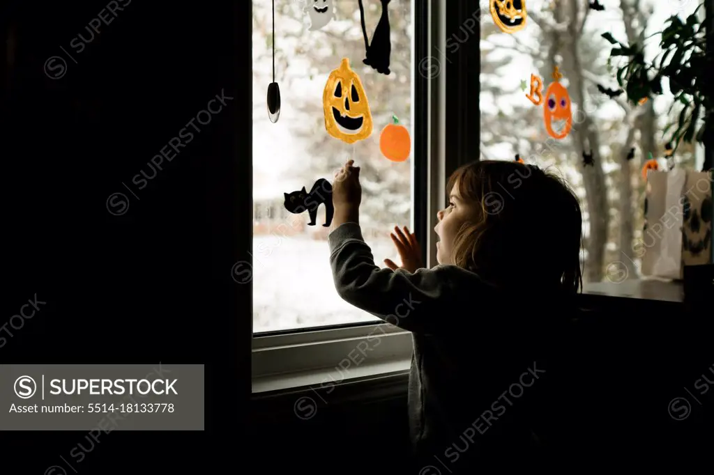 Young girl putting Halloween decorations up on windows in living room