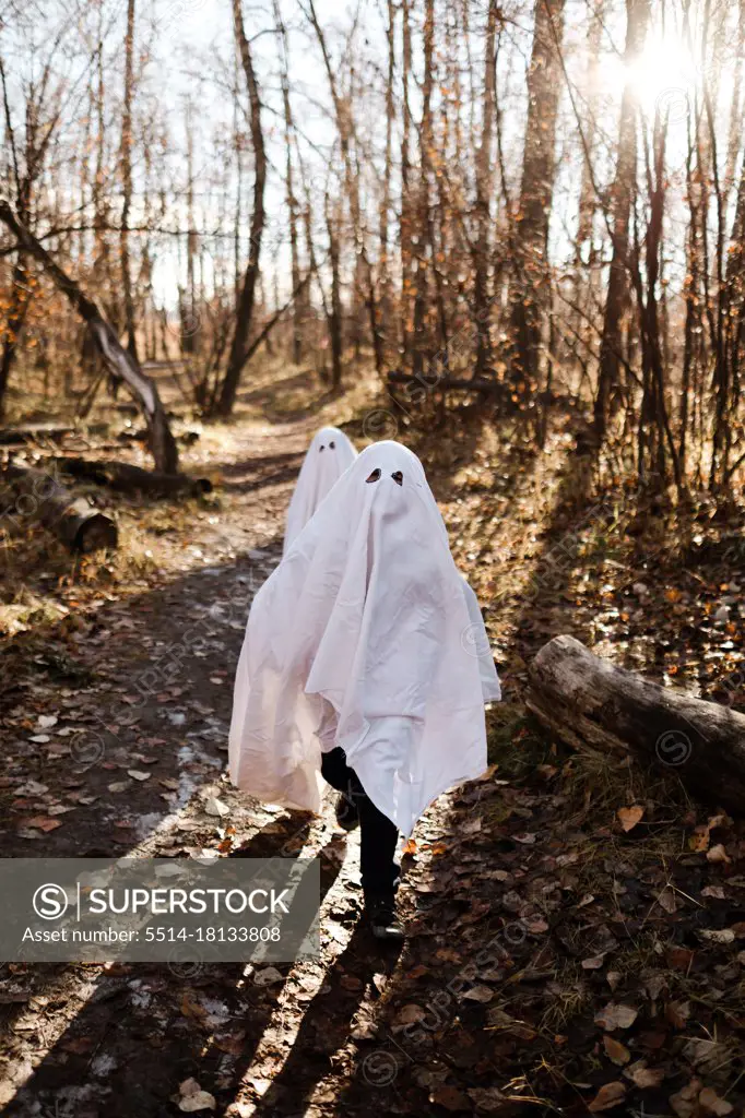 Two children in ghost costumes running in a park in the fall