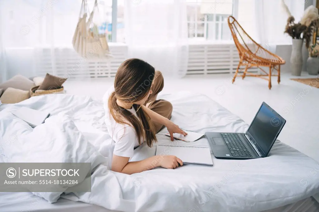 girl writes in a notebook and listens to music in bed