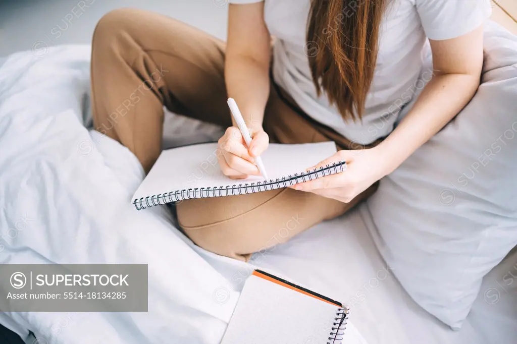 girl writes in a notebook and listens to music in bed