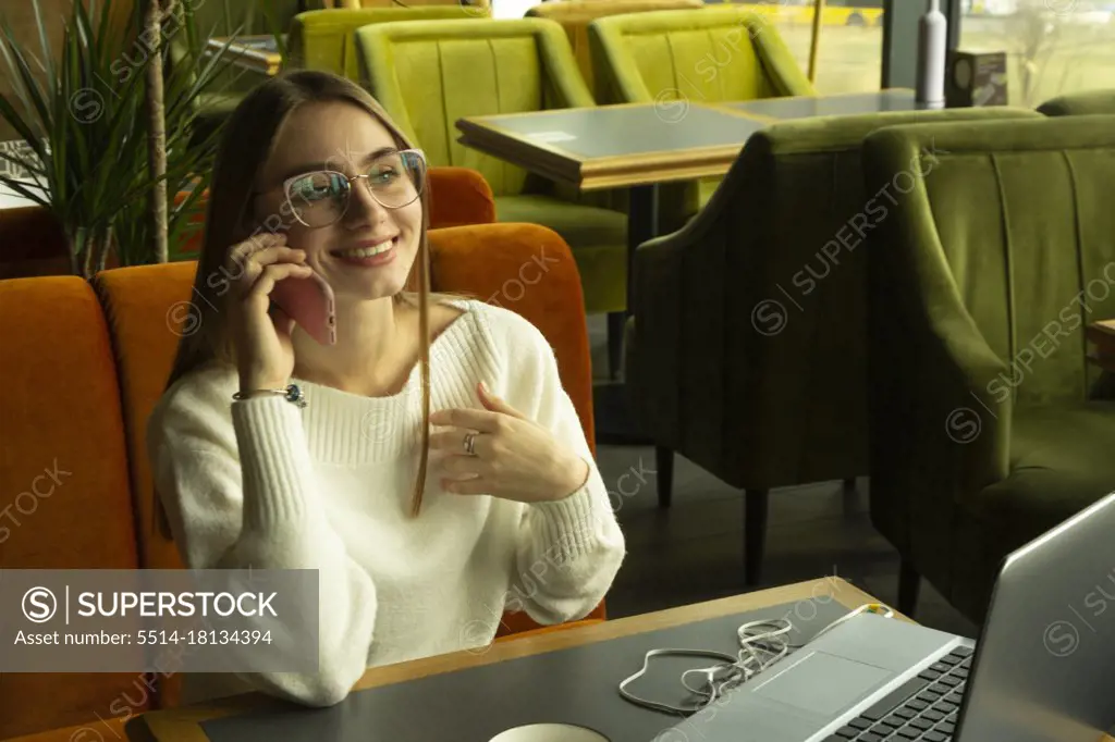 Smiling woman in glasses talking on the cell phone on a sofa in a cafe