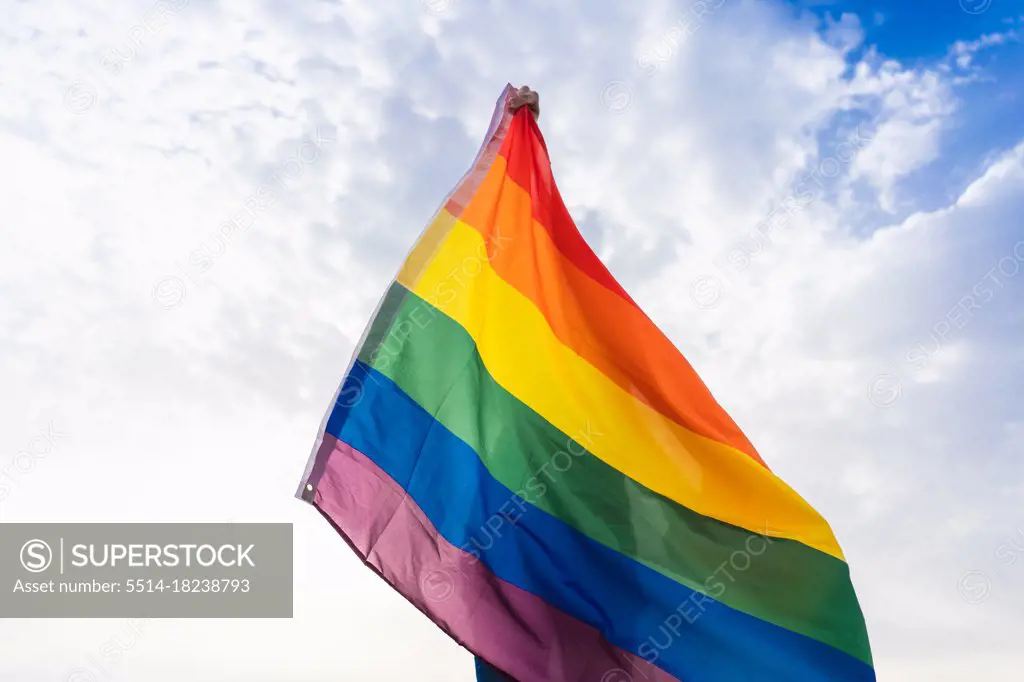 Unknown person posing with LGBT flag covering his body with sky behind